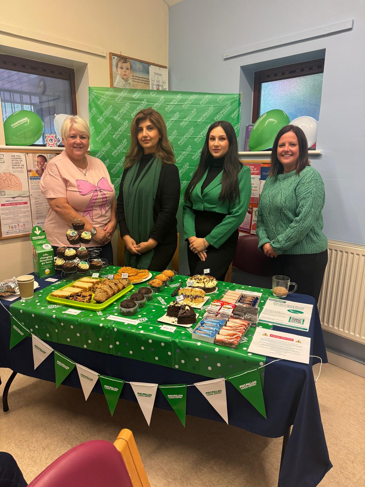 4 members of staff stood behind a table with cakes on